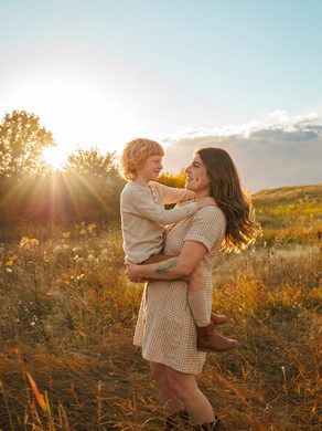 Parent carrying their toddler through a sunlit field