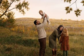 Family of four in a field at sunset, one parent lifting a baby overhead