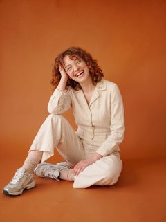 Client seated on the floor of an orange studio backdrop, laughing