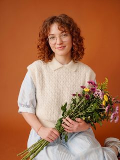 Client in a knit vest holding a wildflower bouquet against an orange studio backdrop