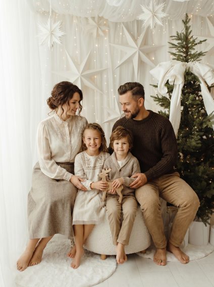 Family of four seated on a white studio set with a Christmas tree and paper stars