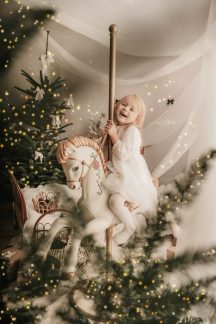 Young child on a rocking horse beside a decorated Christmas tree