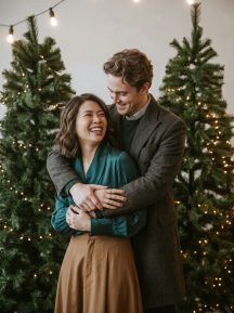 Couple embracing between two lit Christmas trees